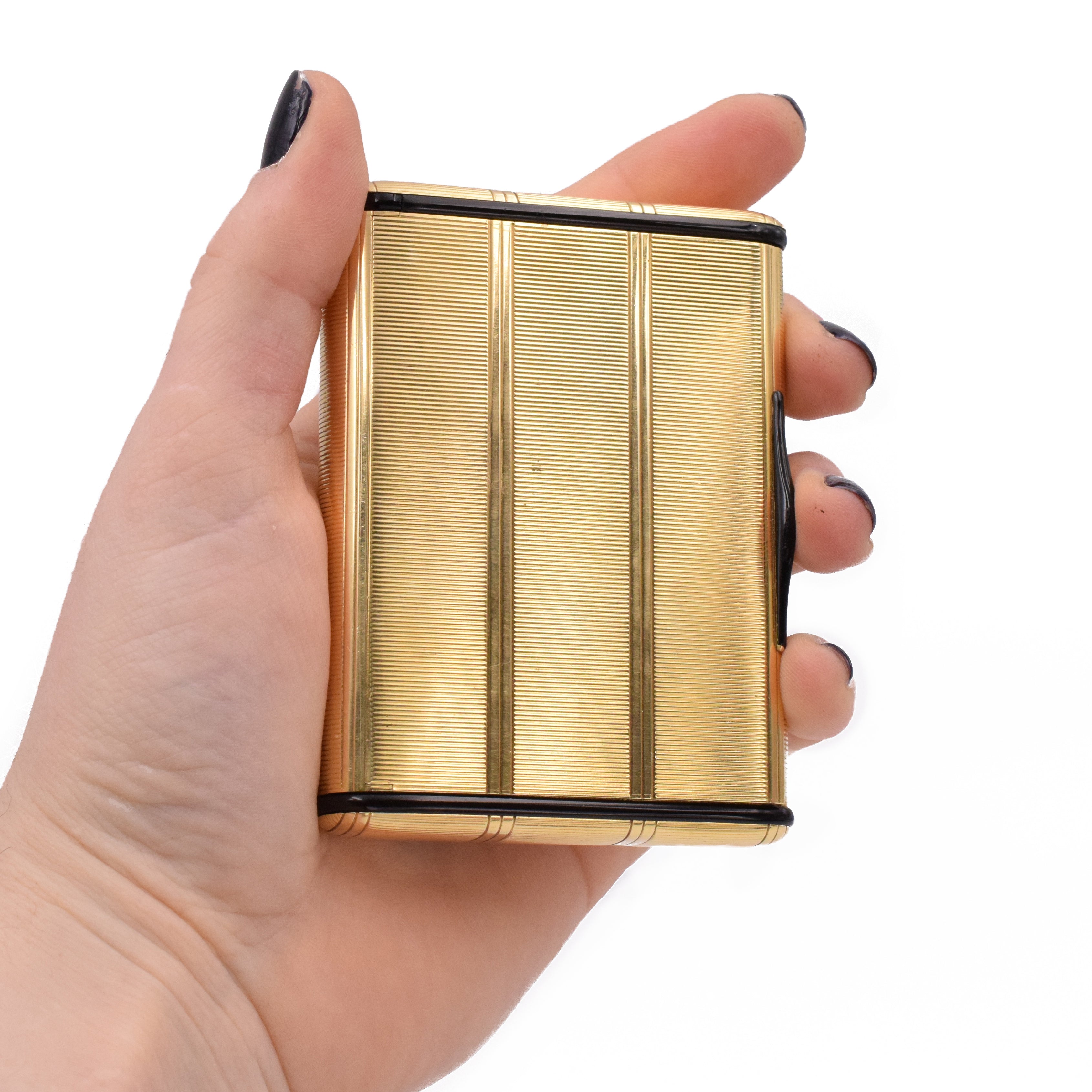 Compact mirror box by Cartier, crafted in 18k yellow gold, beautifully engraved with decorative vertical and horizontal lines throughout the box. Sides of the compact are accented with black onyx shaped into elongated discs with rounded corners, and black enamel on the snap closure lock. Inside equipped with a crystal beveled edge mirror. Measurements 3.5" by 2.6" x 0.6" (89mm x 66mm x 16mm) Signed Cartier and serial number. Stamped 750 for 18k gold. Weight 147.6g. Ref# 950-000-168