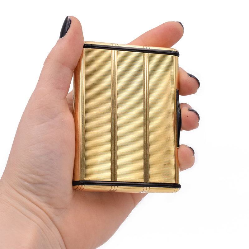 Compact mirror box by Cartier, crafted in 18k yellow gold, beautifully engraved with decorative vertical and horizontal lines throughout the box. Sides of the compact are accented with black onyx shaped into elongated discs with rounded corners, and black enamel on the snap closure lock. Inside equipped with a crystal beveled edge mirror.   Measurements 3.5" by 2.6" x  0.6" (89mm x 66mm x 16mm)  Signed Cartier and serial number.  Stamped 750 for 18k gold. Weight 147.6g.  Ref# 950-000-168